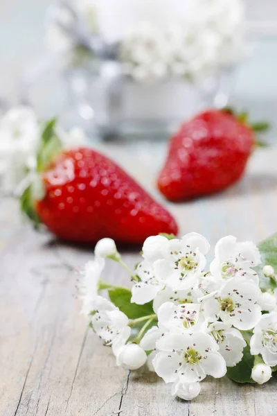 Strawberries and blooming hawthorn flowers on rustic wooden table. Healthy food