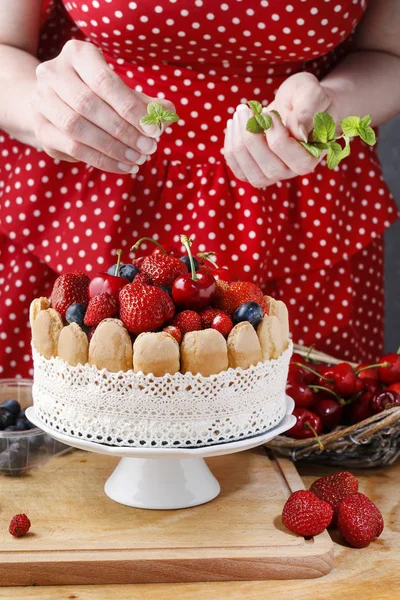 Woman decorating summer sponge cake with fruits on ceramic cake stand. Party dessert