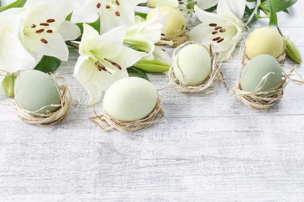 Lírios brancos e ovos de páscoa em fundo de madeira — Fotografia de Stock