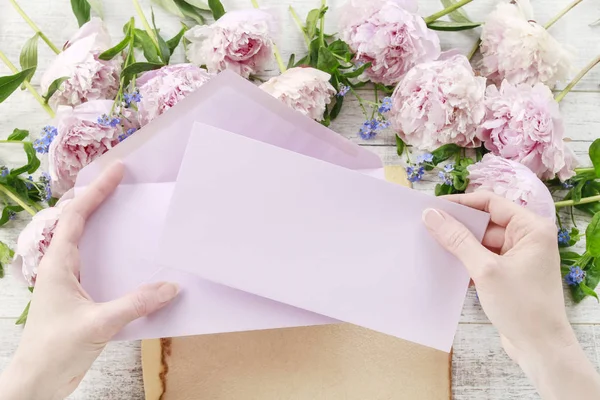 Woman holding pink sheet of paper and envelope.