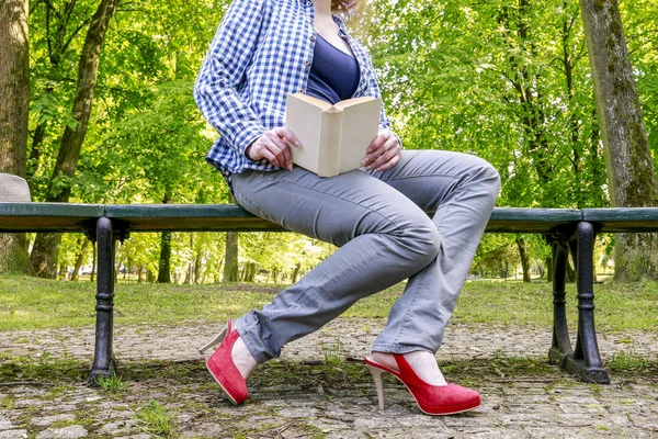 Donna che legge un libro, seduta sulla panchina in un parco — Foto Stock