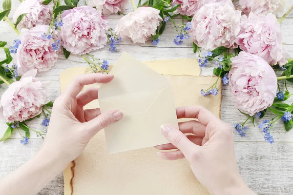 Woman holding small envelope. Pink peonies and forget me not flo — Stock Photo, Image