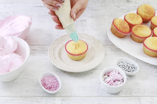 Woman prepares muffins decorated with cream and sprinkles. — Stok fotoğraf