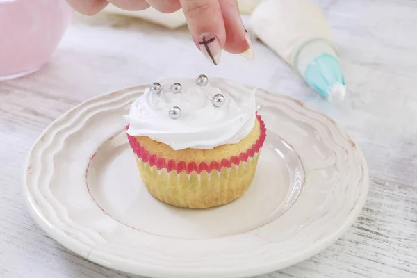 Mujer prepara magdalenas decoradas con crema y espolvoreos . — Foto de Stock