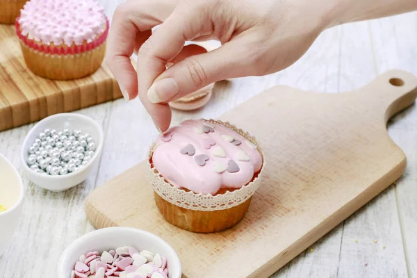 Woman prepares muffins decorated with cream and sprinkles. — Stock Photo, Image