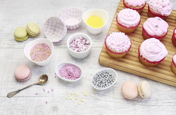 Woman prepares muffins decorated with cream and sprinkles. — Stock Photo, Image