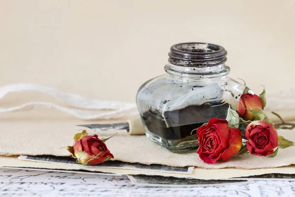 Tintenfass, Stift und getrocknete Rosen auf Vintage-Papier Hintergrund — Stockfoto