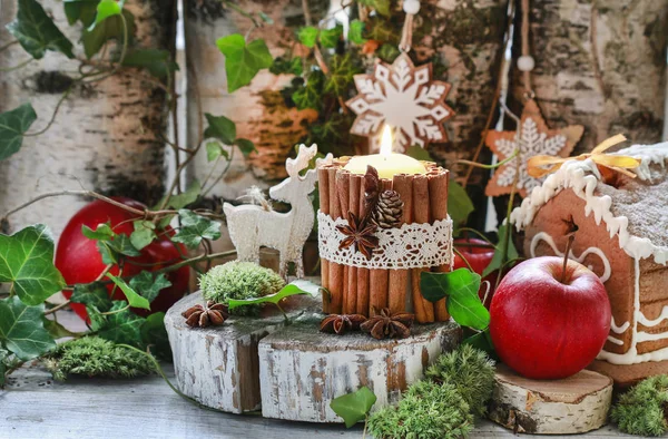 Candle decorated with cinnamon sticks, moss, ivy leaves and wood