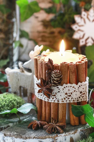 Candle decorated with cinnamon sticks, moss, ivy leaves and wood