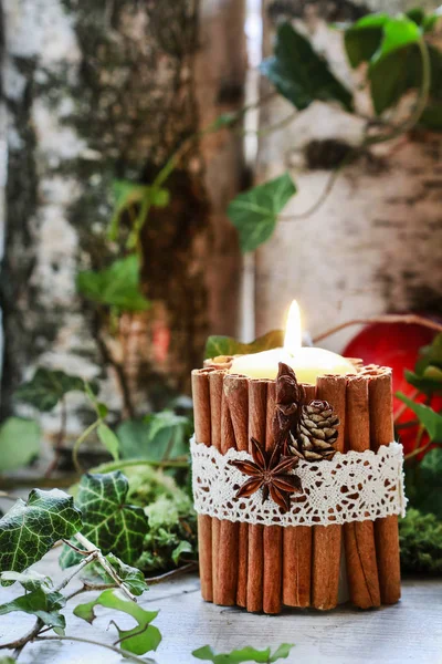 Candle decorated with cinnamon sticks, moss, ivy leaves and wood