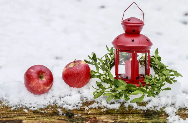 Lanterna rossa, ghirlanda di vischio e due mele sulla neve — Foto Stock