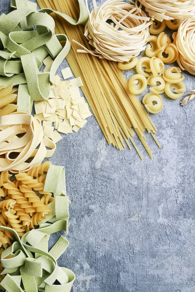 Gemischte Arten und Formen italienischer Pasta auf grauem Stein, Hintergrund — Stockfoto