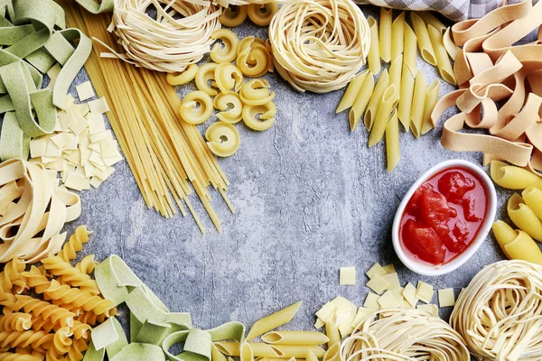 Salsa de tomate en un tazón pequeño y variedad de pasta italiana sobre piedra —  Fotos de Stock