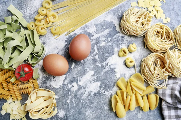 Mixed types and shapes of italian pasta on grey stone, backgroun — Stock Photo, Image