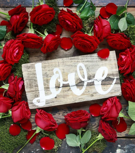 Word love handwritten on wooden board lying among red roses. Val — Stock Photo, Image