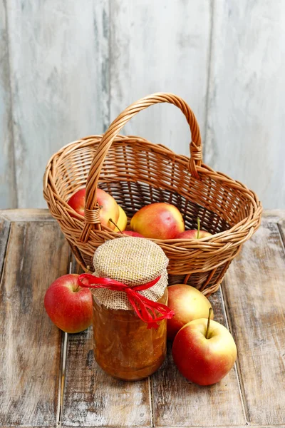 Jar with apple jam and wicker basket with raw fruits. — Stock Photo, Image