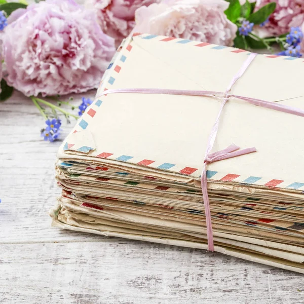 Stack of vintage love letters and pink peonies in the background — Stock Photo, Image