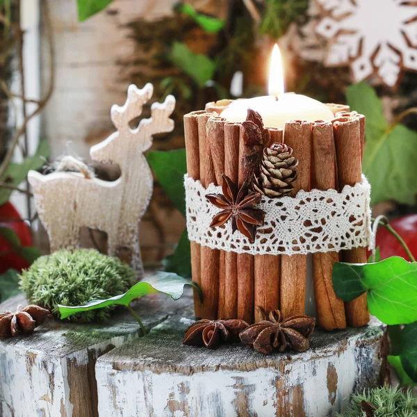 Candle decorated with cinnamon sticks, moss, ivy leaves and wood