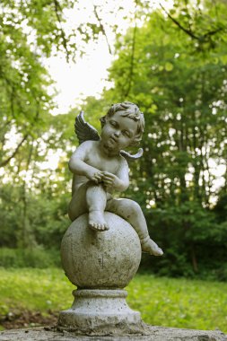 Bahçede taştan yapılmış bebek melek veya cupid figürü.