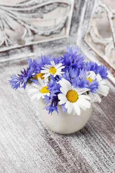 Bouquet of chamomiles and cornflowers on wooden table.