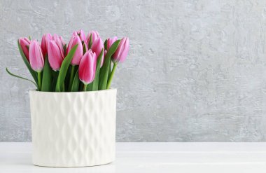 Beyaz seramik vazo, gri taş arka plan pembe laleler. 