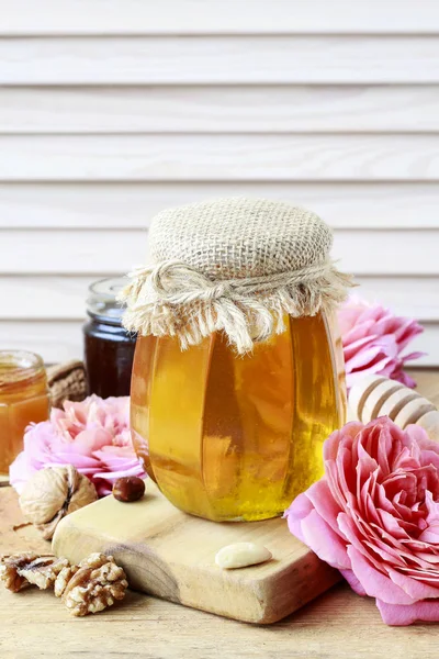 Glass jar of honey among pink roses. — Stock Photo, Image