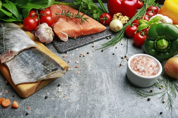 Cod and salmon fillets among colorful vegetables on grey stone b — Stock Photo, Image