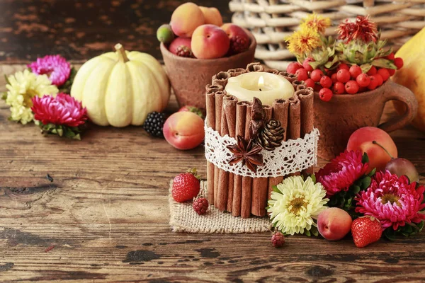 Candle decorated with cinnamon sticks among autumn fruits and fl