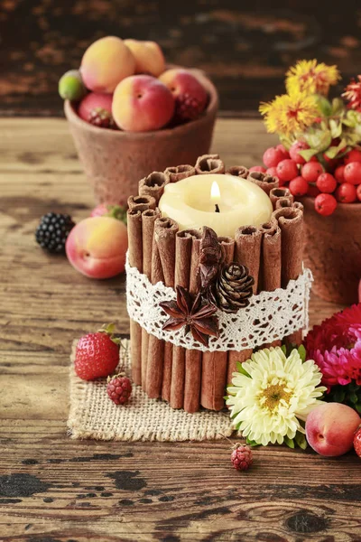 Candle decorated with cinnamon sticks among autumn fruits and fl