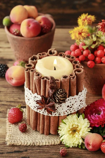 Candle decorated with cinnamon sticks among autumn fruits and fl — Stock Photo, Image