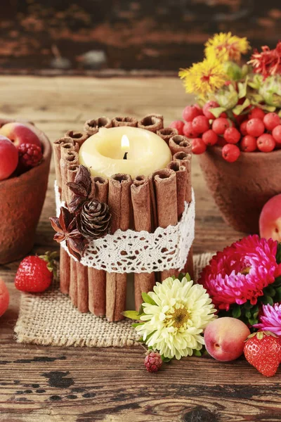 Candle decorated with cinnamon sticks among autumn fruits and fl