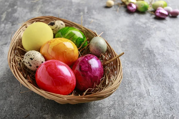 Basket of colorful Easter eggs on grey, stone background. — Stock Photo, Image