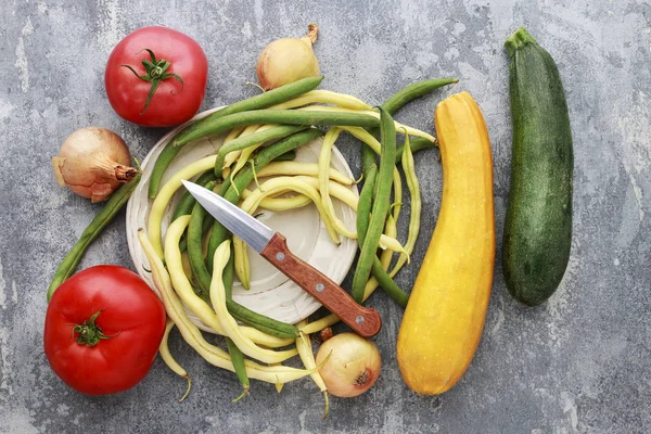 Barevná zelenina a nůž na šedém kamenném pozadí. — Stock fotografie
