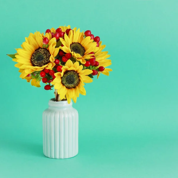 Bouquet of sunflowers and hypericum berries in mint ceramic vase