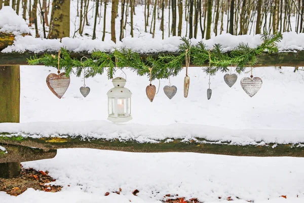 Ghirlanda di abete, lanterna di ferro e cuori di legno appesi in inverno ga — Foto Stock