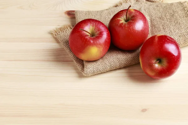 Rode appels op jute zak, houten achtergrond. — Stockfoto