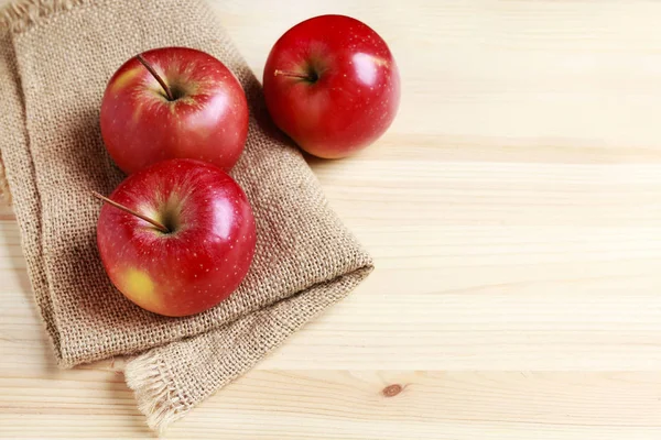 Красные яблоки на джуте мешок, деревянный фон . — стоковое фото