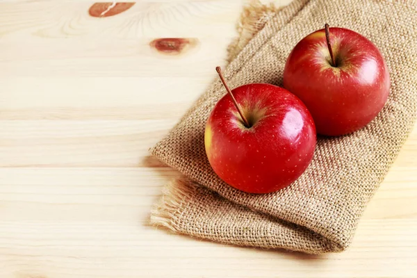 Manzanas rojas sobre saco de yute, fondo de madera . — Foto de Stock