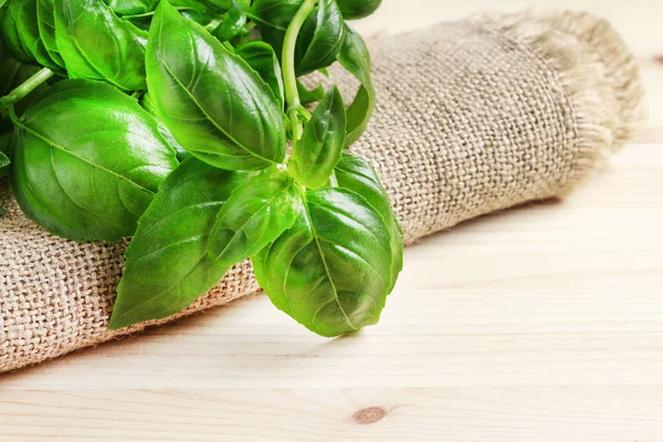 Basil leaves on jute sack, wooden background — Stock Photo, Image