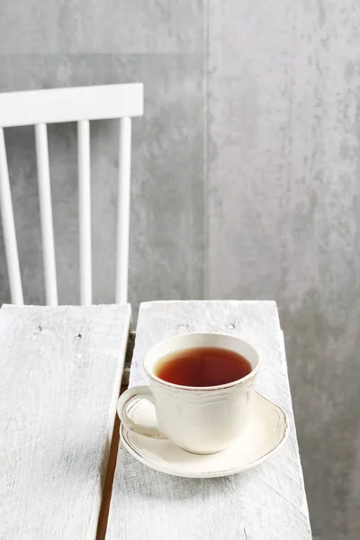 Ένα φλιτζάνι τσάι σε ξύλινο τραπέζι. Καρέκλα στο παρασκήνιο. — Φωτογραφία Αρχείου