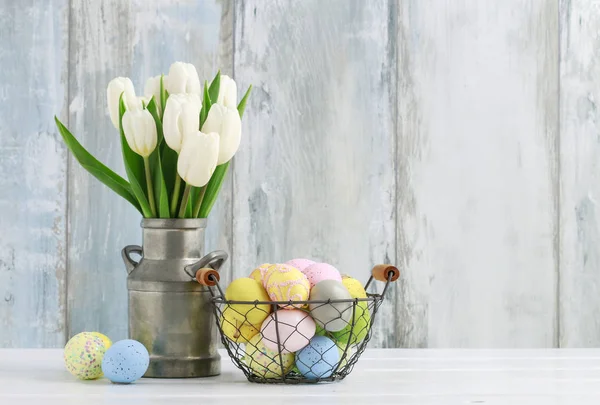 Basket with Easter eggs and bouquet of white tulips in siver can — Stock Photo, Image