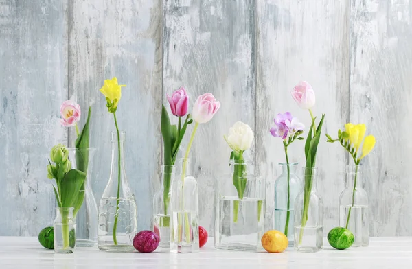 Colorful flowers in glass bottles and Easter eggs on the table
