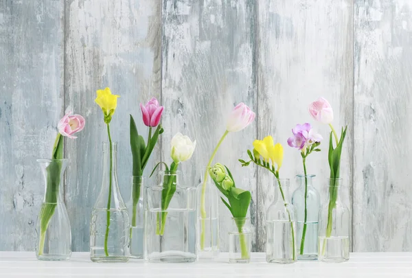 Flores coloridas em garrafas de vidro e ovos de Páscoa na mesa — Fotografia de Stock