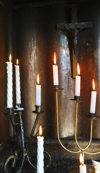 Bílé svíčky hoří ve staré svatyni. Kříž s Ježíšem na stěně. — Stock fotografie