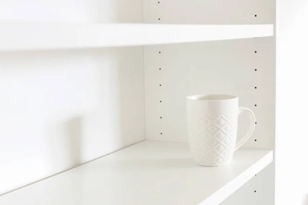 A white ceramic mug standing on an empty shelf. — Stock Photo, Image