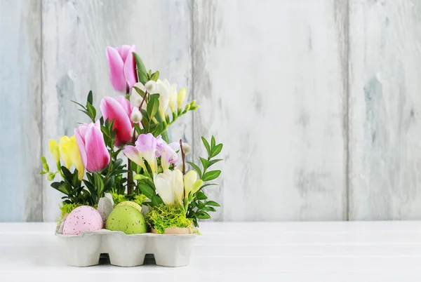 Velikonoční květinové dekorace s pestrými vejci, tulipány, frézie — Stock fotografie