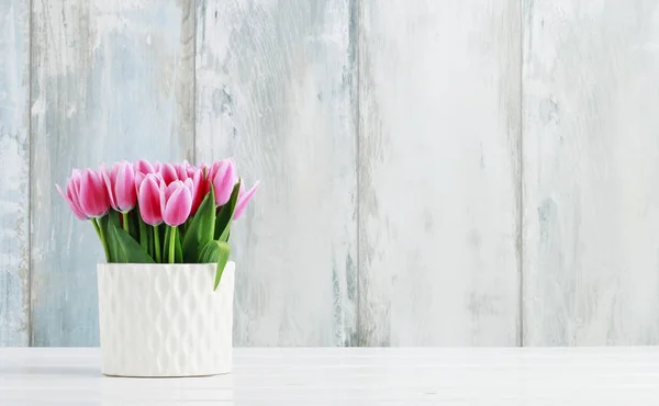 Růžové tulipány v bílé keramické váze, dřevěné pozadí. — Stock fotografie