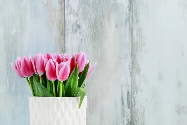 Tulipas rosa em vaso de cerâmica branca, fundo de parede de madeira . — Fotografia de Stock