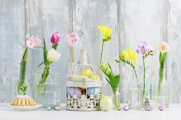 Colorful flowers in glass bottles and Easter eggs in vintage bir