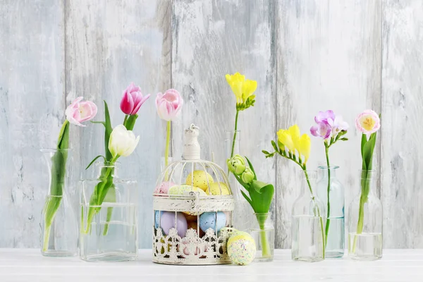 Flores coloridas en botellas de vidrio y huevos de Pascua en bir vintage —  Fotos de Stock